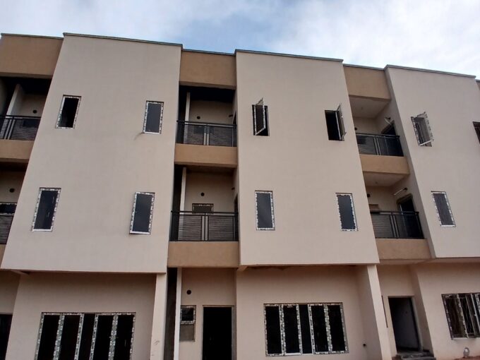 Facade view of a newly constructed multi-story residential building with open windows and unfinished landscaping.